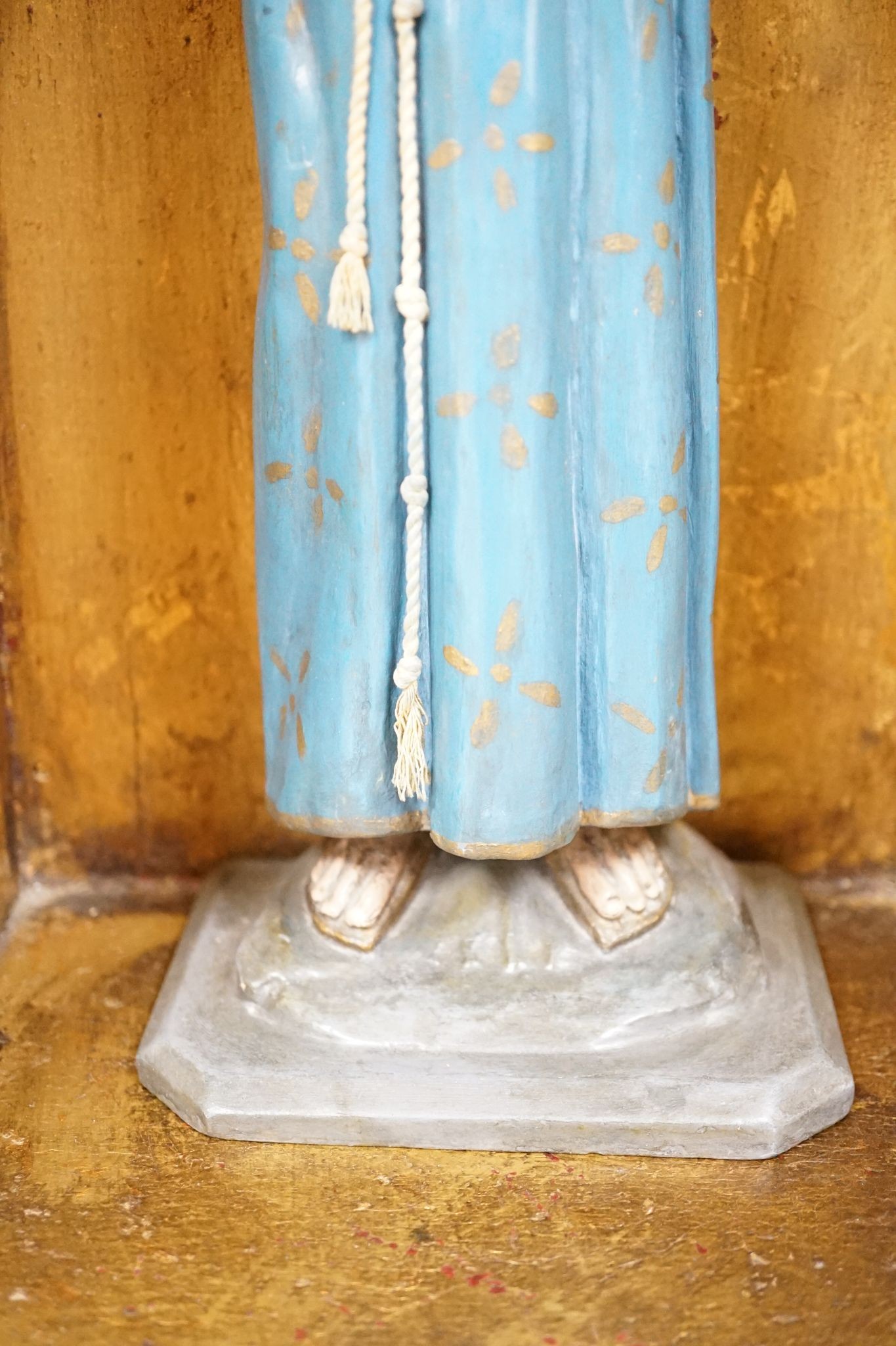 A painted saint with a blue robe and gilt metal halo, standing in an ornate carved niche, 57cm